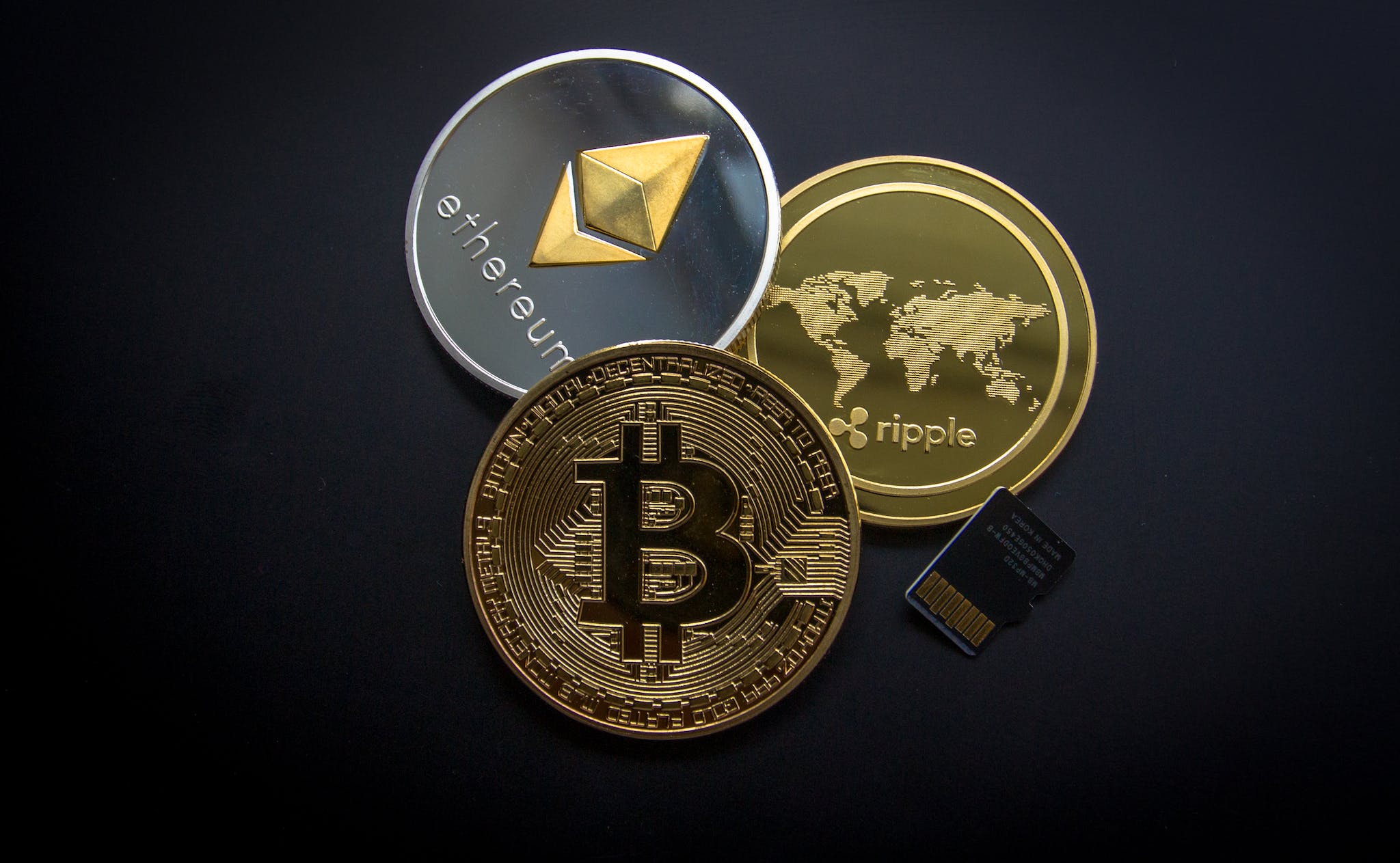 bitcoin, ethereum, ripple coins and sd card on dark surface.
